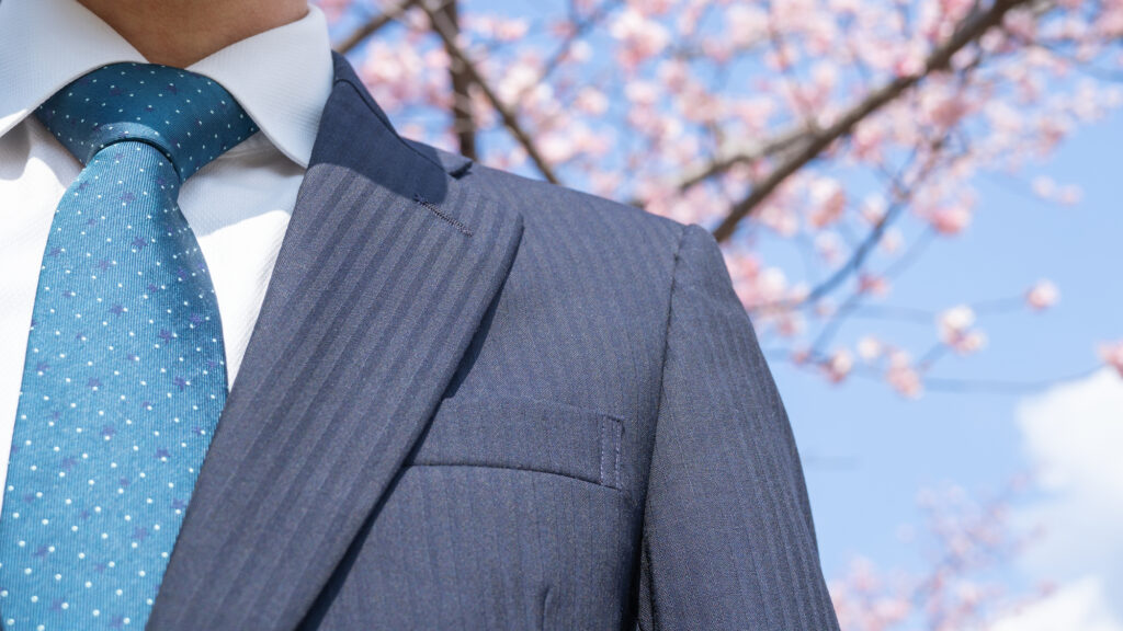 桜の前に立つスーツの男性の上半身